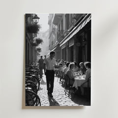 Charming Street Café Poster från Bozetto visar en svartvit scen av ett livligt utomhuscafé med gäster, en servitör och cyklar på en kullerstensgata - perfekt att visa på premiumpapper.
