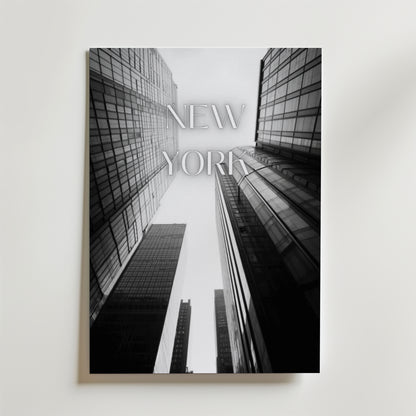 Bozetto New York Poster föreställer svartvita skyskrapor tagna från en låg vinkel med "NEW YORK" i transparenta bokstäver, tryckt på FSC-certifierat premiumpapper för en miljövänlig touch.