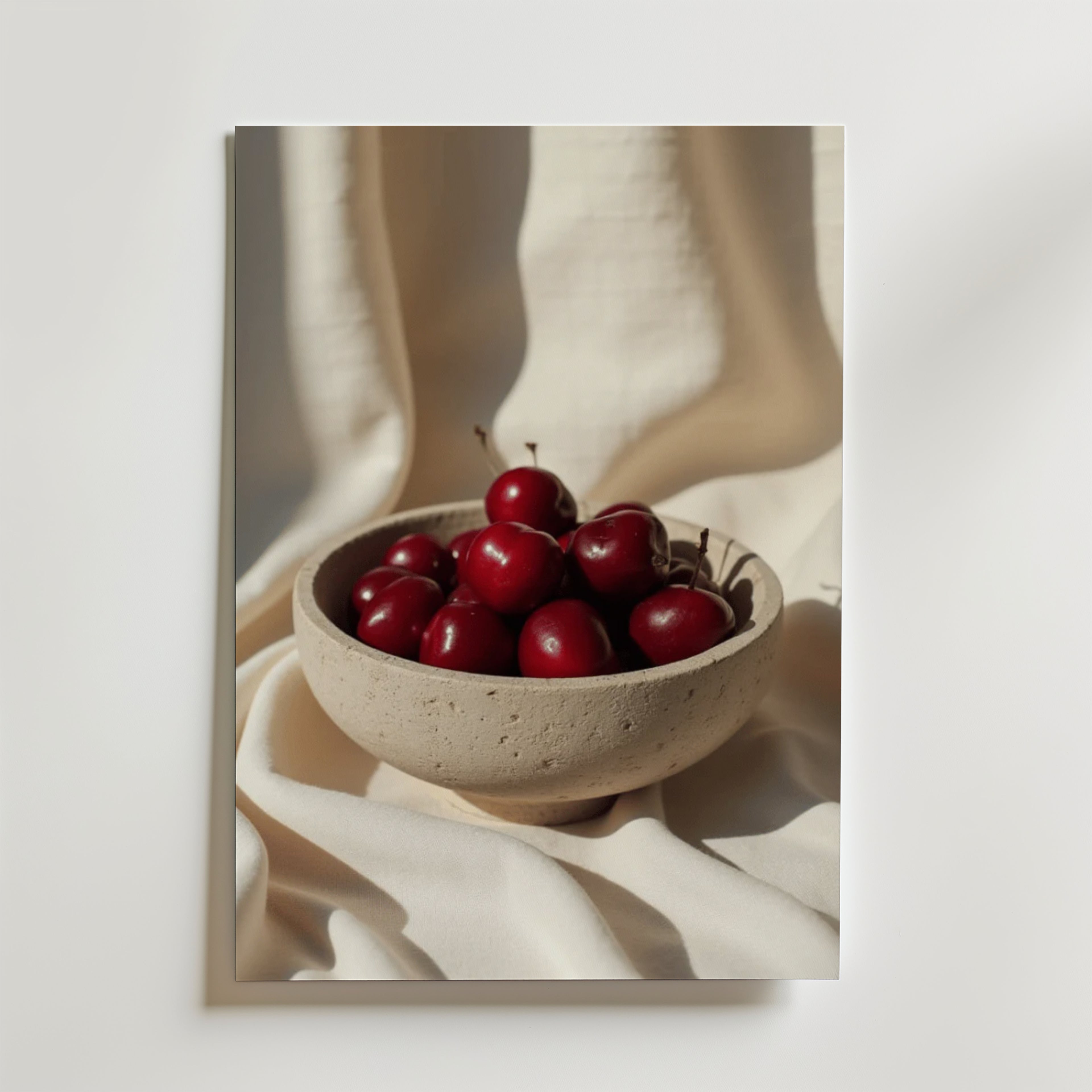 Ceramic Cherry Poster från Bozetto föreställer en beige keramikskål med röda körsbär på ett mjukt vitt tyg som framhäver den matta ytan i svagt ljus. Postern är tryckt på premiumpapper och ger en lugn, minimalistisk touch till ditt rum.