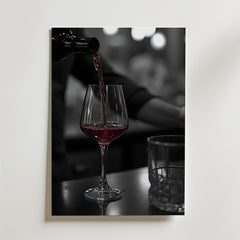 Bozetto Pouring Passion Wine Poster visar rött vin som hälls upp i ett glas på en mörk yta bredvid ett tomt glas, med mjukt suddiga bokeh-ljus som förstärker skönheten i vin i rörelse.