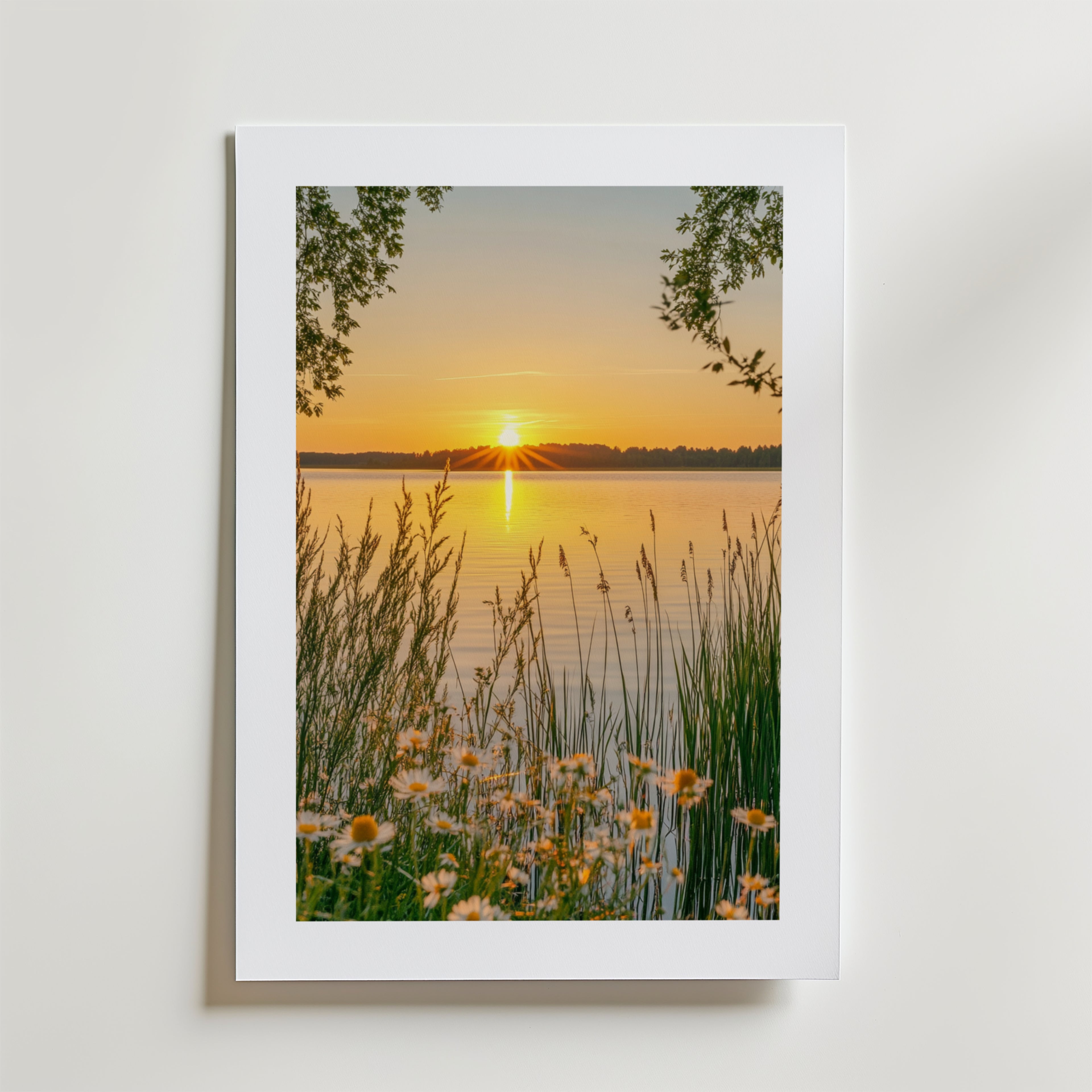 Golden Hour By The Lake Poster by Bozetto föreställer en lugn sjökant i solnedgång med högt gräs, vildblommor och trädgrenar på FSC-certifierat premiumpapper med högkvalitativ finish.