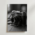 Bozetto Old School Camera Poster föreställer ett svartvitt foto av en vintage filmkamera på trä mot en enfärgad bakgrund - perfekt för alla som vill ha en nostalgisk touch i sin inredning.