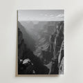 Grand Canyon Shadows Poster by Bozetto: Svartvitt foto med karga klippor och en skuggig dal under en delvis molnig himmel, tryckt på FSC-certifierat premiumpapper med elegant matt yta. Perfekt som Grand Canyon väggkonst.