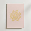 Golden Bloom on Blush Poster by Bozetto är en minimalistisk konstprint med ett guldgult, blomliknande mönster av detaljerade bladliknande kronblad på ljusrosa, som visas på en ljus yta.