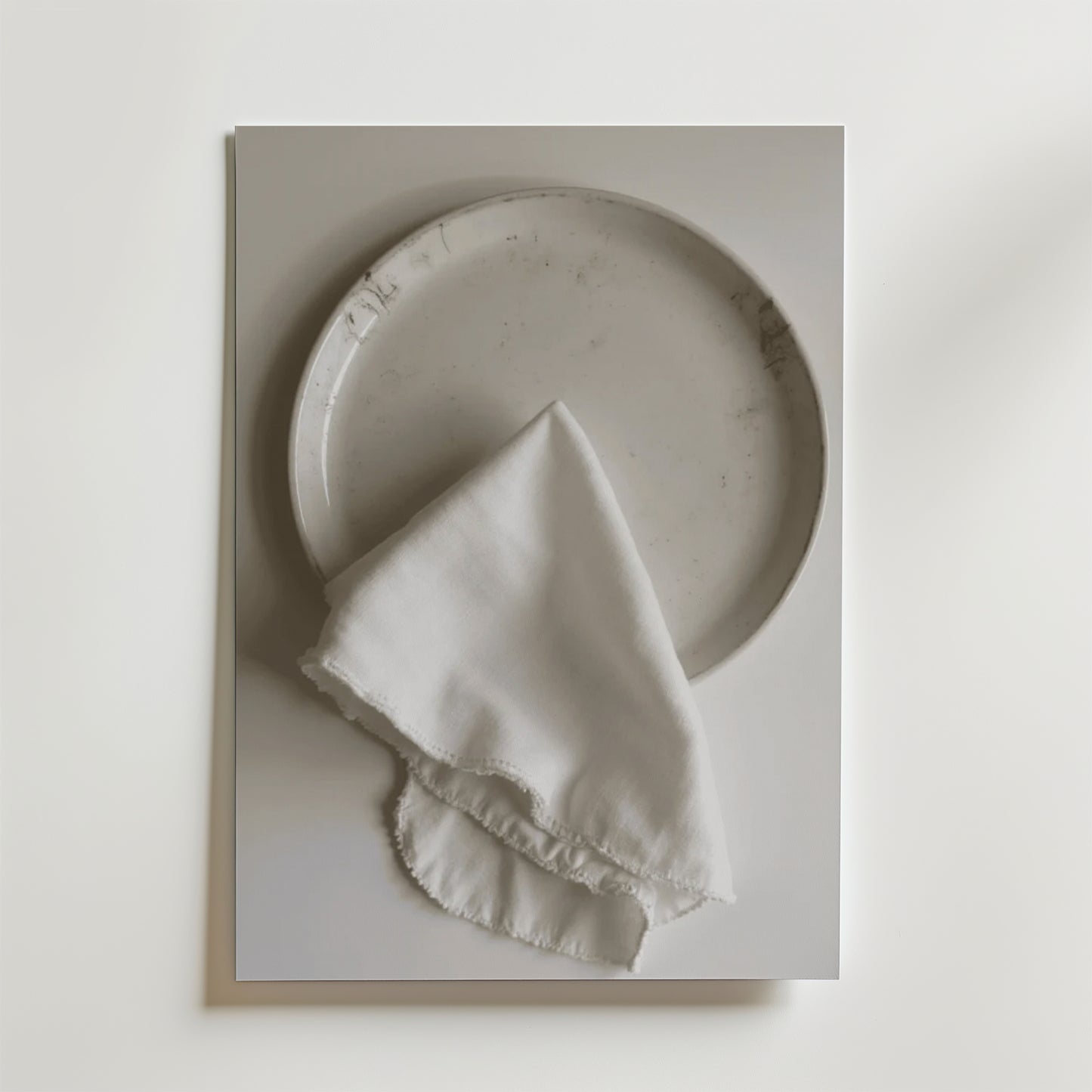En Bozetto White linen dinner napkin Poster visar en vit keramiktallrik som toppas med en fransig vit linneservett, allt mot en vit bakgrund med en lyxig matt finish.