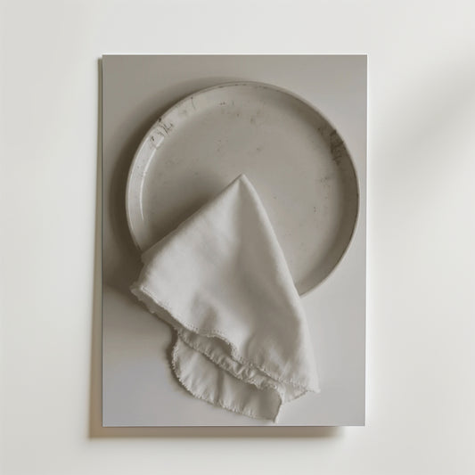 En Bozetto White linen dinner napkin Poster visar en vit keramiktallrik som toppas med en fransig vit linneservett, allt mot en vit bakgrund med en lyxig matt finish.