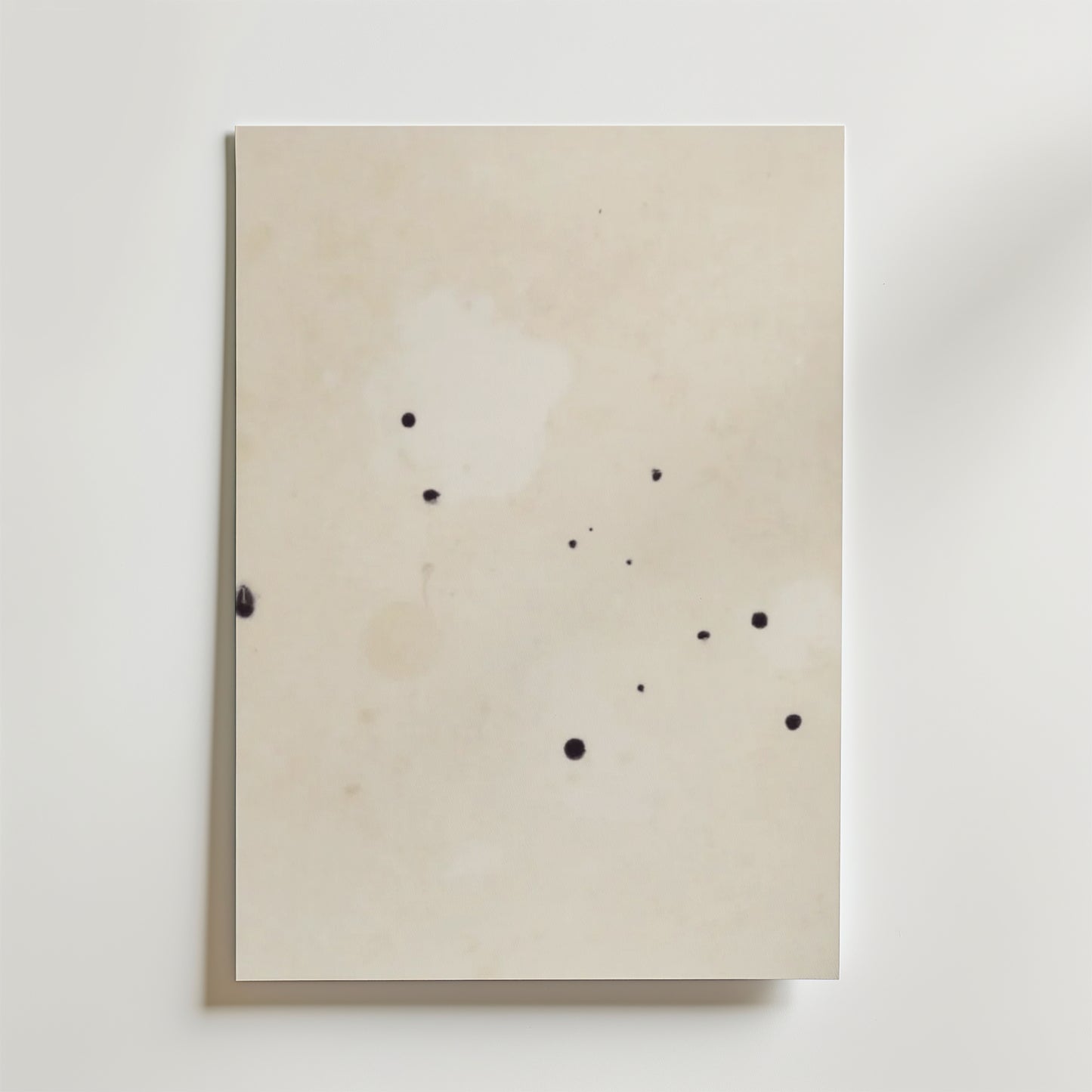 Postern Abstract Beige No.2 Poster by Bozetto har ett off-white premiumpapper med små, oregelbundna svarta bläckfläckar på den matta ytan, fotograferat mot en vit bakgrund.