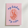 Bozetto My Kitchen My Rules Poster har en central röd räkillustration, omgiven av blå kursiv "my kitchen my rules" i rosa dekorstil, och är avbildad lutad mot en vit yta.