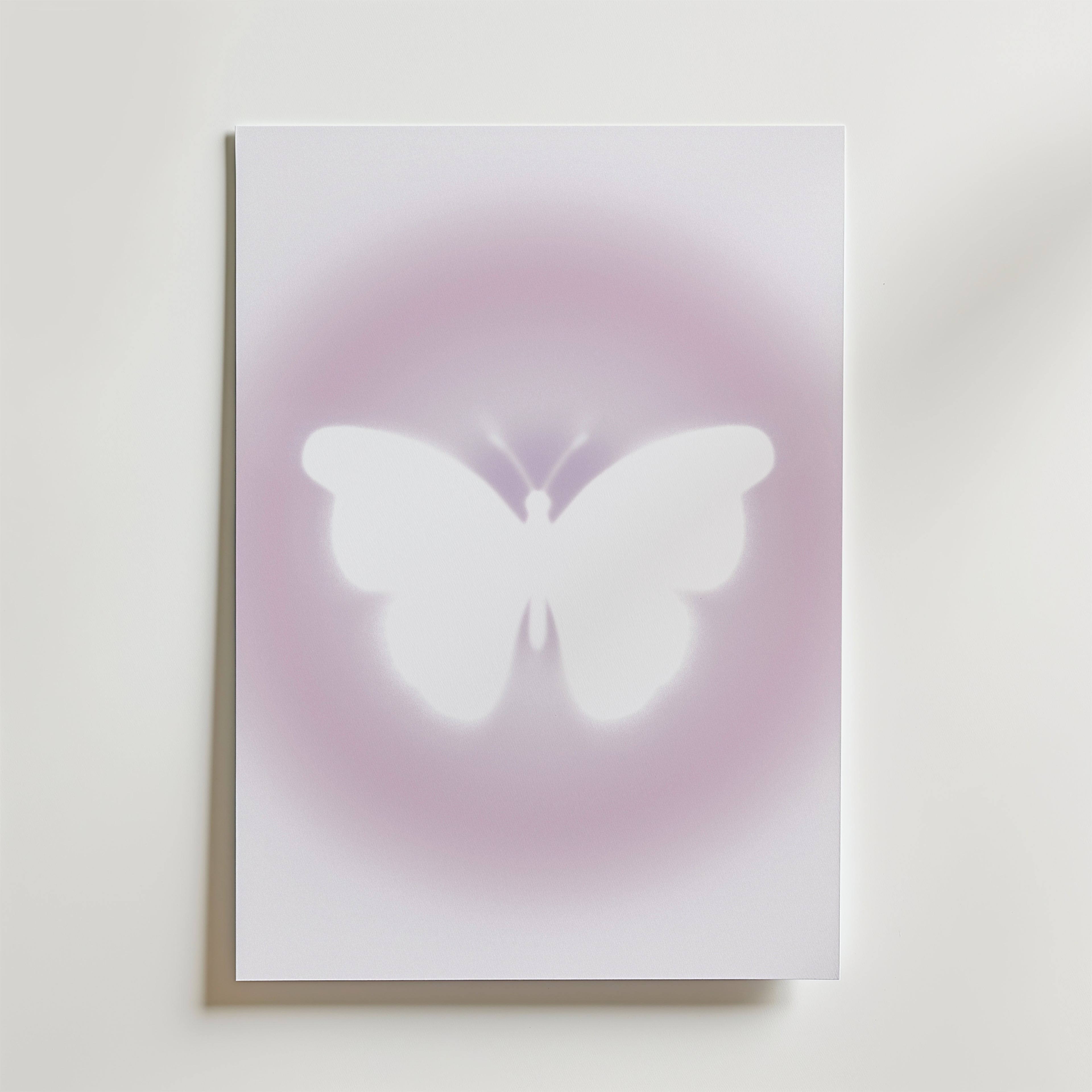 Bozetto's Soft Glow Butterfly Poster visar en vit fjäril i silhuett centrerad mot en ljus, minimalistisk bakgrund med drömskt rosa-lila sken.