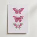 Postern Pink Butterfly Trio Poster från Bozetto föreställer tre illustrerade fjärilar i rosa och mintgrönt staplade vertikalt på en vit bakgrund, vilket framhäver deras unika vingmönster och eleganta skönhet.