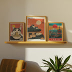 Bozettos Bundle 3-pack Japandi No. 6 innehåller inramade tavlor: en katt som äter nudlar, katter på ett tak i Tokyo med en röd sol och en stadsbild i Tokyo med pagoder, alla i japandistil - solljuset kastar skuggor över en stol och en växt nedanför.